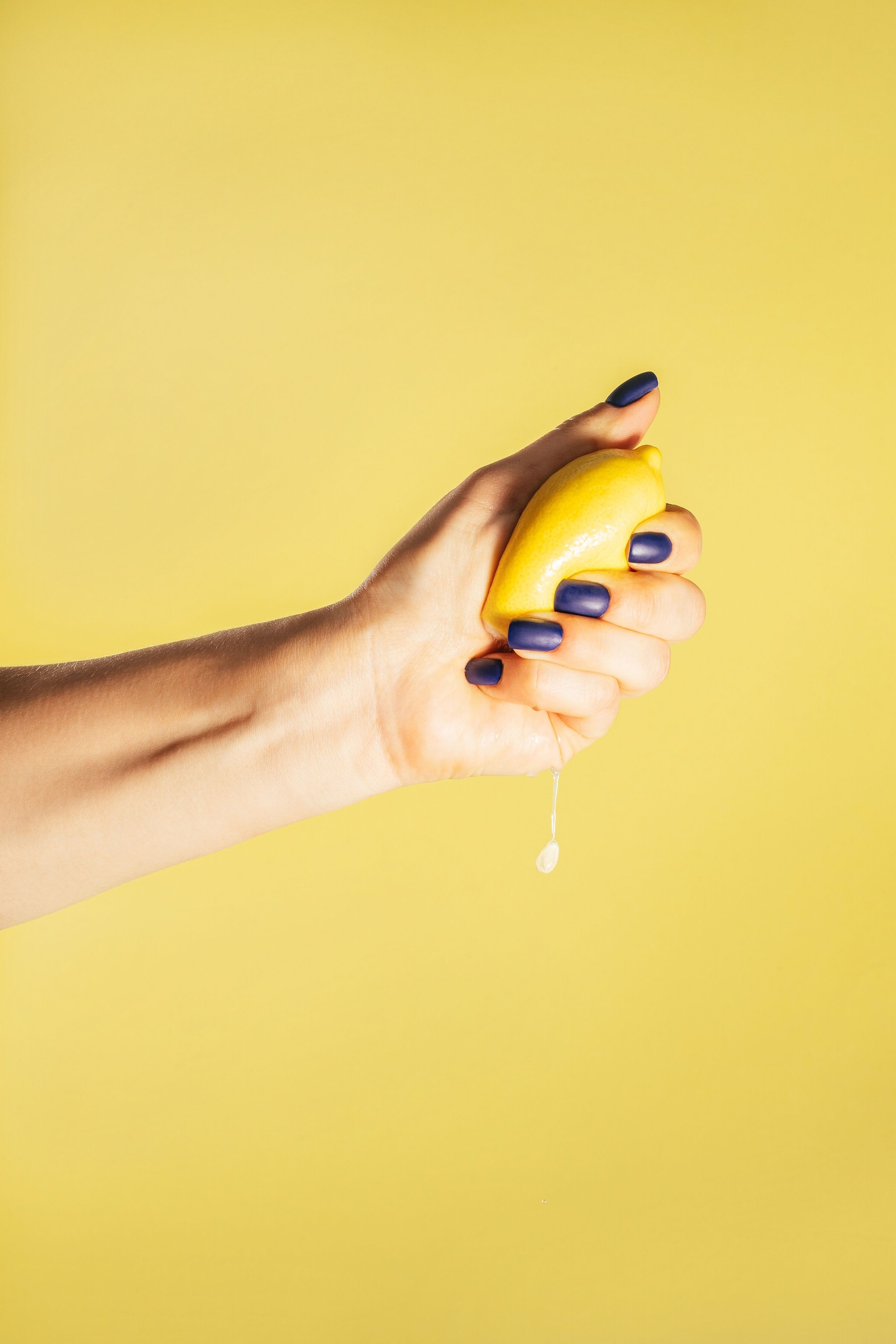 Female hand with blue nails hold fresh lemon isolated on yellow. Squeeze out juice. Finger crush. Vertical, copy space