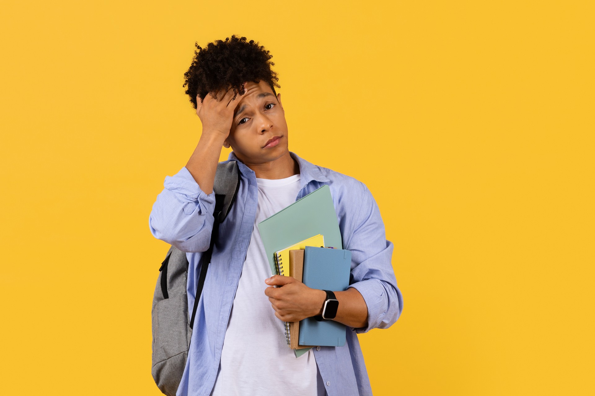 Pensive black student with books on yellow, hand on head